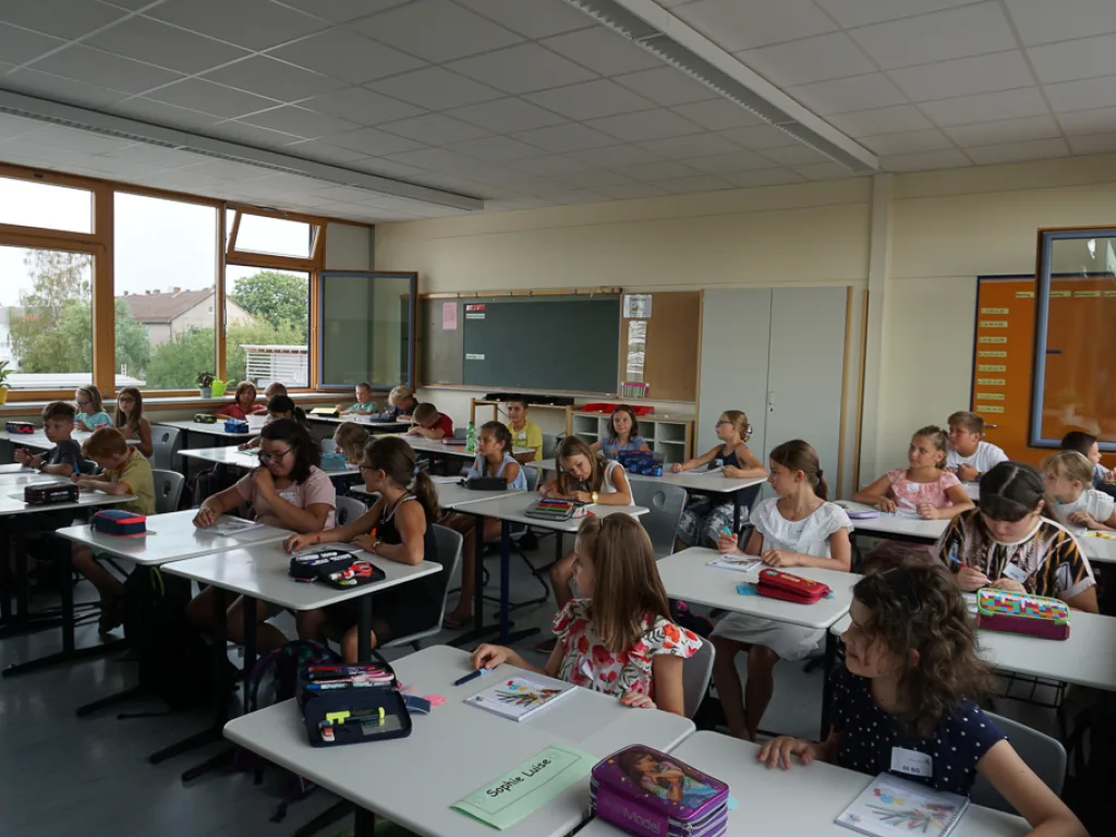 Kinder arbeiten an Tischen im hellen Klassenraum.